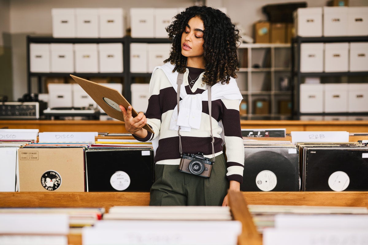 A woman holds up a record in a record store with the Nikon Z f around her neck